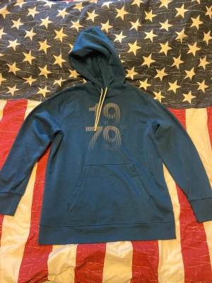 Blå hoodie med tryck 1979 - Säljer en blå hoodie med trycket '1979' framtill och vita snören i huvan. Tröjan har känguruficka och är fodrad med mjuk fleece på insidan. Perfekt för dig som gillar en avslappnad och stilren look. Storlek M. Tröjan är använd i väldigt gott skick. 