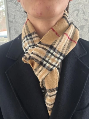 Burberry Scarf (ÄKTA) -  Snygg beige halsduk från Burberry med klassiskt rutigt mönster. Halsduken har fransar i ändarna och är tillverkad i mjuk ull som känns skön mot huden. Perfekt att slänga runt halsen för en stilren look.  ✅ Skick: 8/10 🧵Material: Fin lamm-ull 🎨 Färg: Beige (med vita, svarta och röda detaljer) ✨Väldigt skön, tidlös och snygg halsduk med fint material   ‼️Skickas samma dag eller dagen efter köpet genomförs‼️ 