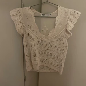 Beige spetsblus från Zara - Säljer en superfin beige blus från Zara med spetsdetaljer och volang vid axlarna. Blusen har v-ringad hals och är ärmlös med broderade mönster och luftig stickad känsla. Perfekt för dig som gillar romantisk och boho stil!