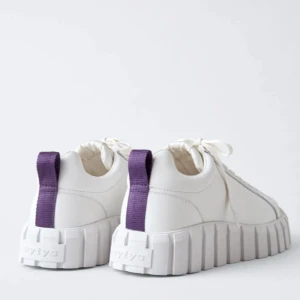 Eytys vita sneakers med plattform - Säljer ett par vita sneakers från Eytys med chunky plattformssula och lila dragflik bak. Skorna har snörning och en rund tå, tillverkade i skinn med detaljer i syntet. Perfekt för dig som gillar statement-skor och vill sticka ut med cool design.