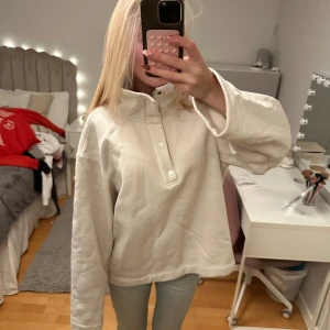 Vit fleece-tröja med halv dragkedja - Mysig vit fleece-tröja med halv dragkedja och tryckknappar i halsen. Tröjan har en bred krage med fluffigt foder och långa, lite oversized ärmar. Perfekt för kyliga dagar och har en loose passform som ger en chill vibe.