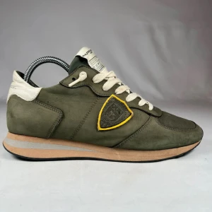 Philippe Model gröna sneakers - Snygga sneakers från Philippe Model i olivgrönt med beige detaljer och vit snörning. Skorna har en rund tå, platt sula och ett coolt tygmärke med gul kant på sidan. Materialmix av mocka och textil ger en schysst känsla och stilren look.