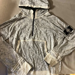 Stone Island hoodie med half zip - Säljer en gråmelerad hoodie från Stone Island med svart logotyp-patch på ärmen. Tröjan har huva, half zip framtill och en stor magficka. Materialet är mjuk bomull och passformen är normal. Perfekt för dig som gillar streetwear och snygga detaljer. Finns ej att köpa längre. 100% äkta. 
