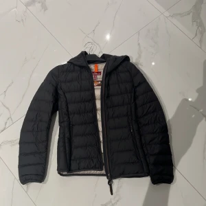 Svart dunjacka från Parajumpers S - Svart dunjacka från Parajumpers i storlek S. Jackan är superlätt, har huva, två sidofickor med dragkedja och quiltad design. Insidan är ljusgrå och jackan har en snygg orange detalj vid nacken. Perfekt för kalla dagar och riktigt stilren. Pris kan diskuteras vid snabb affär!