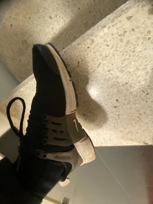 Nike Presto svarta sneakers - Nike Presto sneakers i svart med grå detaljer och vit sula. Skorna har en rund tå, snörning och en syntetisk ovandel med mesh för extra komfort. Snyggt Nike-logga på sidan och tå. Perfekt för dig som gillar sportig och clean stil.