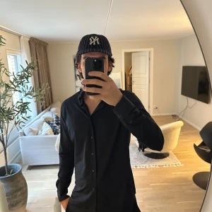 Svart Xacus Active Shirt Tailor Fit - Svart långärmad skjorta från Xacus, modell Active Shirt Tailor Fit. Skjortan har klassisk krage, knappar framtill och är tillverkad i ett stretchigt, andningsbart syntetmaterial som torkar snabbt. Snygg och stilren passform som sitter riktigt bra.