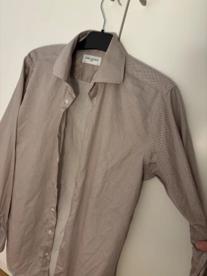 Beige rutig skjorta från John Henric - Snygg beige skjorta från John Henric med diskret rutigt mönster och klassisk krage. Skjortan har vita knappar och lång ärm, perfekt för dig som gillar stilrena detaljer. Materialet är mjuk bomull.