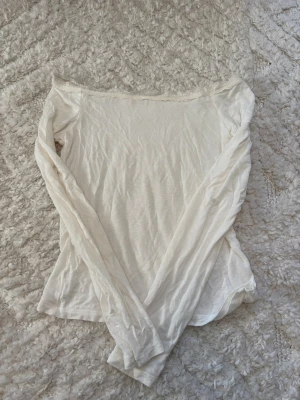 Vit långärmad offshoulder topp - Säljer en vit långärmad topp med offshoulder-design och smal spetskant upptill. Tunn och mjuk i materialet, perfekt för dig som gillar en enkel och clean look. Säljer pågrund av att den inte kommer till användning.