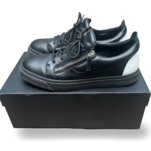 (Äkta) Vit/Svarta Giuseppe Zanotti Skor - Jag säljer dessa otroligt fräscha Giuseppe Zanotti Frankie sneakers. Inga skador på skorna. Skorna är självklart äkta och sparsamt använda, mycket fint skick. Nypris ligger på över 6000kr. Dessa fungerar fint både till fest och vardag. Storlek 43. Box och dustbag medföljer.