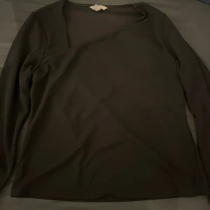 Svart asymmetrisk topp från H&M - Svart långärmad topp från H&M i storlek XL med snygg asymmetrisk halsringning. Passar som en M. Perfekt för dig som gillar stilrena och moderna plagg med en twist.