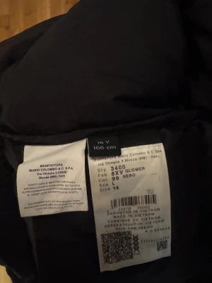 Svart glansig dunjacka från Colmar - Säljer en svart, glansig dunjacka från Colmar med huva och dragkedja framtill. Jackan har en puffad look och är tillverkad i syntetmaterial med dunfyllning. Perfekt för dig som vill ha en varm och snygg jacka med cool streetstil.