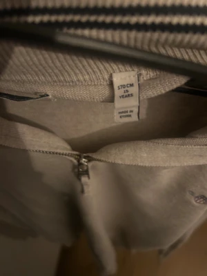 Beige half zip tröja från GANT - Snygg beige långärmad tröja från GANT med ribbad hög krage och half zip-dragkedja framtill. Diskret GANT-logga broderad på bröstet. Mjuk bomullskvalitet och klassisk passform som funkar till många stilar.