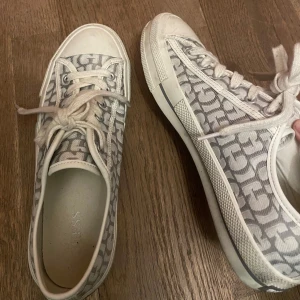 Guess sneakers - Snygga sneakers från guess med klassiskt monogrammönster i grått och vitt. Skorna har rund tå, platt sula och vita snören. Perfekta för dig som gillar stilrena och trendiga detaljer. Materialet är textil med gummisula. Använda fåtal gånger därav lite smutsiga men går super enkelt att tvätta bort! 💗