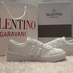 Valentino Rockstud vita sneakers - Säljer ett par sjukt snygga vita Valentino Rockstud sneakers i skinn. De har ikoniska nitar längs sidorna och bak på sulan, samt coola detaljer på plösen. Klassisk rund tå och platt sula, perfekt för dig som vill sticka ut med stilrena men edgy skor.