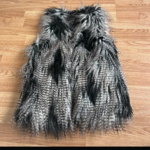 Fluffig svartgrå pälsväst - Säljer en riktigt fluffig och cool pälsväst i svart och grå toner. Västen har ett mönstrat, nästan randigt utseende med långa, mjuka hårstrån och fodrad insida i svart tyg. Köpt på sellpy och original lappen är borta så vet ej vilket märke eller storlek men skulle säga att den passar S/M