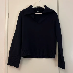 Mörkblå stickad tröja Gina Tricot XS - Snygg mörkblå stickad tröja från Gina Tricot i storlek XS. Tröjan har en bred krage, v-ringad hals och ribbade detaljer vid krage, ärmslut och nederkant. Perfekt för dig som gillar en chill och stilren look.