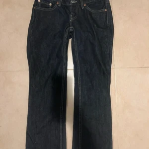 Lågmidjade Levi's 501 mörkblå jeans bootcut - Snygga lågmidjade mörkblå Levi's 501 jeans med klassisk femficksdesign och kontrastsömmar. Modellen har bootcut-ben och normal passform, tillverkade i slitstarkt jeanstyg. Säljer då de blivit för små för mig.