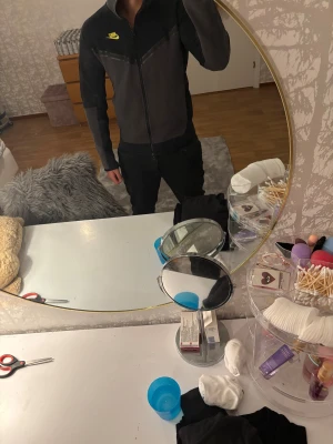  mörkgrå nike tech vindjacka med huva - Säljer en snygg mörkgrå nike tech som huva  huva och hel dragkedja. Jackan har en neon gul Nike-logga på bröstet och en praktisk ficka med dragkedja på ärmen. Perfekt för dig som gillar sportig stil och vill ha något som funkar året runt.