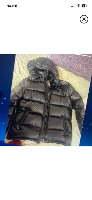 Svart pufferjacka från Moncler - Säljer en svart pufferjacka från Moncler med huva och dragkedja framtill. Jackan har en glansig finish, breda quiltade sektioner och praktiska fickor med dragkedja. Perfekt för kalla dagar och har en riktigt snygg streetstil.