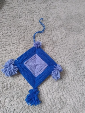 Blå handgjord drömfångare i garn - Handgjord drömfångare i mörkblått och ljusblått garn i fyrkantig form. Den har pompoms på kanterna och går att fästa med hjälp av ett blått snöre. Superfin inrednings detalj för den som gillar unik och färgglad inredning.