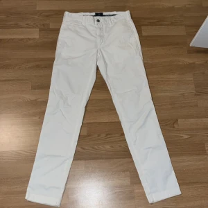 Vita chinos från Morris TM - Snygga vita byxor från Morris TM med klassisk passform och raka ben. Byxorna har knapp och dragkedja framtill samt fickor på sidorna. Perfekta för en clean och fräsch look. Materialet är mjuk bomull som känns skönt mot huden.