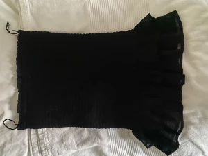 Svart volangkjol från Bik Bok XS - Supersöt svart kortkjol från Bik Bok i smockat tyg med volangkant nertill. Kjolen har en tight passform och är perfekt för dig som gillar en enkel men ändå trendig look. Resår i midjan för extra komfort. Går även att använda som en topp