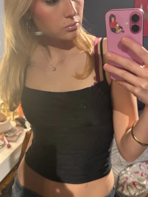 Svart glittrig linnetopp - Säljer en svart linnetopp med tunna axelband och diskreta glittriga detaljer upptill. Toppen har en tight passform och är ärmlös. 