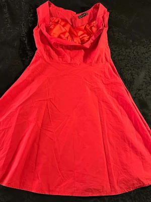 Röd kortklänning från iHot - Snygg röd klänning från iHot i storlek L med ett glansigt tyg upptill och en bred krage. Klänningen är ärmlös och har en dragkedja i ryggen. Passformen är normal och kjolen är utsvängd för en feminin siluett.