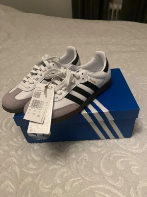 Adidas Samba OG sneakers vit/svart - Adidas Samba OG sneakers i klassisk vit och svart färg med de ikoniska tre ränderna på sidan. Min syster köpte och var för små helt nya och oanvända