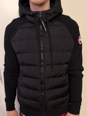 Canada Goose Hybridge Huron Jacket  - Säljer en HYBRIDGE HURON FULL ZIP HOODY jacket från Canada Goose. jackan är som ny och har endast varit använd ett fåtal gånger. 