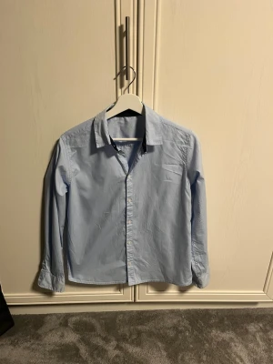 Ljusblå skjorta i bomull - Klassisk ljusblå skjorta med krage och knappar framtill. Tillverkad i 100% bomull för en skön och luftig känsla. Långärmad modell som passar perfekt till jeans eller chinos. Enkel och stilren design utan mönster. Skick 10/10 + extra knappar på köpet! Vid frågor är det bara att höra av sig! 