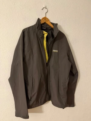 Grå vindjacka från Peak Performance - Snygg grå vindjacka från Peak Performance med gul detalj på insidan och logga på bröstet. Jackan har hög krage, dragkedja framtill och långa ärmar. Perfekt för blåsiga dagar och har en clean, sportig look.