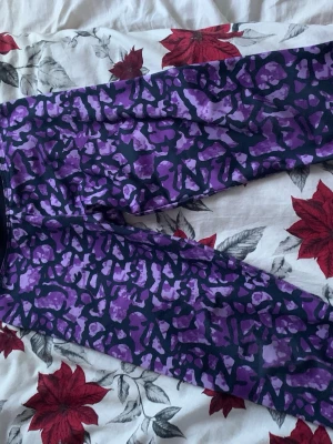 Lila mönstrade träningsleggings PXS - Säljer ett par träningsleggings från Phelix Sports i storlek 134/140. De har ett coolt lila och svart leopardmönster och är gjorda i ett stretchigt syntetmaterial som passar perfekt för träning. Snygga och bekväma för dig som gillar färg och mönster.