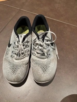 Nike Free RN grå sneakers - Grå Nike Free RN sneakers med svart swoosh och vit sula. Ovandelen är i mesh för extra andningsförmåga och skon har snörning. Perfekta för träning eller vardagsstil. Lätta och flexibla med platt sula och rund tå.