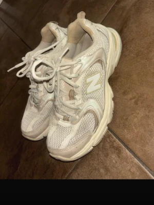 New Balance 530 sneakers beige/vit - Säljer ett par New Balance 530 sneakers i beige och vit med mesh och syntetmaterial. Skorna har rund tå, platt sula och snörning. Ikonisk N-logga på sidan och bekväm dämpning i sulan. Perfekta för dig som gillar retrostil och sportig vibe.