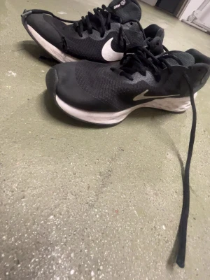 Svarta Nike sneakers med vit sula - Säljer ett par svarta Nike sneakers med vit sula och klassisk vit swoosh på sidan. Skorna har snörning och är tillverkade i mesh och syntetmaterial för bra andningsförmåga. Perfekta för träning eller vardagsbruk.