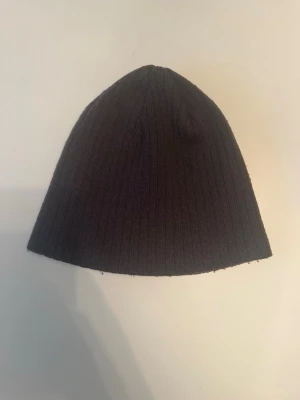 Mörkgrå ribbad mössa från Trend Eagle för ungdomar - En mörkgrå, ribbstickad mössa från Trend Eagle. Klassisk och enkel design i one size som passar ungdomar. Tillverkad i 100% akryl.