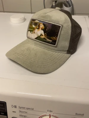 Beige och brun keps från Maggiore - Snygg keps från Maggiore i beige och brunt med mesh på sidorna och baksidan. Framsidan har en patch med retroinspirerat motiv. Kepsen har justerbar snapback och är tillverkad i mjukt material framtill och mesh baktill för extra ventilation.