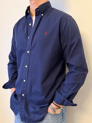 Mörkblå skjorta från Ralph Lauren - En snygg polo skjorta som passar till alla tillställningar! Klassisk mörkblå med röd logga som aldrig går fel. Passform Casual-fit.  Storlek👔: M Nypris💰: ca 1399 kr