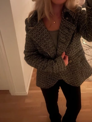 Svartvit rutig jacka med knappar - Säljer en svartvit jacka med rutigt mönster och stora knappar framtill. Jackan har en klassisk krage och är långärmad. Materialet känns tjockt och mjukt, perfekt för kyligare dagar. Snygg att styla med jeans eller svarta byxor.