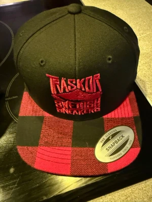 Snapback Träskor Swedish Sneakers [röd brodyr] - Snapback keps med logo ”Träskor Swedish Sneakers” i färg svart med röd brodyr samt röd/svart rutig skärm. Helt ny aldrig använd. Nypris 389 kr i web butik.