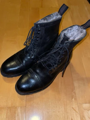 Svarta fodrade kängor Roberto Ley - Säljer ett par svarta kängor från Roberto Ley med snörning och grov sula. Det är hand tillverkade skor av äkta läder i Spanien. De är använda en gång ute men är annars i nytt skick.Insidan är fodrad med mjuk päls för extra värme. Skorna är tillverkade i skinn och har rund tå samt praktiska dragflikar baktill. Perfekta för kalla dagar och vinterväder. Priset är inte hugget i sten. Skriv vid minsta fråga!