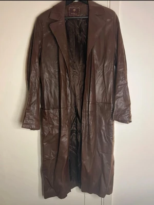 Brun lång skinnkappa från Mulberry - Säljer en brun lång skinnkappa från Mulberry med klassisk krage och hel längd. Jackan har en stilren design och är tillverkad i mjukt skinn. Perfekt för dig som vill ha en tidlös och cool look. Storlek 14 ca M