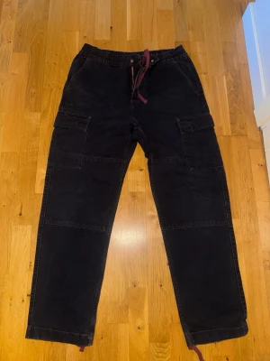 Carhartt keyton cargo byxor M - Säljer ett par svarta Carhartt Keyton cargo pants i storlek M. Byxorna har flera praktiska fickor på sidorna, elastisk midja med snörning och raka ben. Materialet är 100% bomull vilket gör dem både slitstarka och bekväma. Perfekta för en avslappnad streetwear-look.