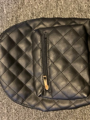 Svart quiltad mini ryggsäck med gulddetaljer - Säljer en svart quiltad mini ryggsäck med snygga guldfärgade dragkedjor och detaljer. Väskan har ett stort huvudfack, en mindre ficka framtill och justerbara axelremmar. Materialet är skinnimitation och insidan har en extra ficka med dragkedja.