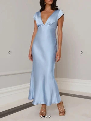 Ljusblå långklänning med öppen rygg - Säljer en elegant ljusblå långklänning i satinliknande material med v-ringad front och korta ärmar. Klänningen har en snygg öppen rygg med twistad detalj och figurnära passform som ger en stilren siluett. Perfekt för bal eller andra fina tillställningar . Har använts 1 gång till studentbalen, och är i bra skick förutom att en tråd har släppt på underdelen av klänningen. Kan skicka bild vid förfrågan. Pris kan diskuteras.