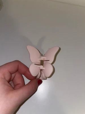 Léonie Rosa fjärils hårklämma - Säljer en superfin hårklämma från Leonie i ljusrosa färg, formad som en fjäril. Klämman har mjuka, rundade kanter och ett stadigt metallfjäderfäste. Perfekt för att sätta upp håret på ett gulligt sätt och ge frisyren lite extra vibe☺️✨
