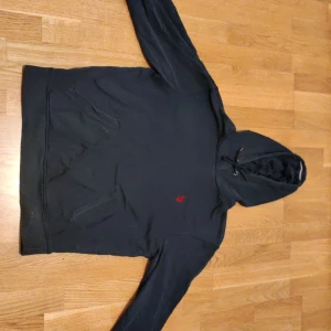 Svart hoodie från U.S. Polo Assn M - Svart hoodie från U.S. Polo Assn. i storlek M. Klassisk modell med huva och snörning, känguruficka framtill och röd broderad logga på bröstet. Perfekt för chill dagar och enkel att matcha med jeans eller joggers.