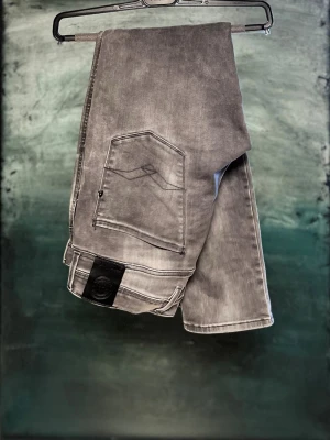 Replay Anbass grå jeans, stl 32 - Säljer ett par Replay Anbass jeans i grå tvättad färg. Modellen har fem fickor, svarta detaljer och klassisk Replay-logga på bakfickan. Jeansen är raka med normal passform och tillverkade i mjukt bomullsmaterial med lite stretch för extra komfort.