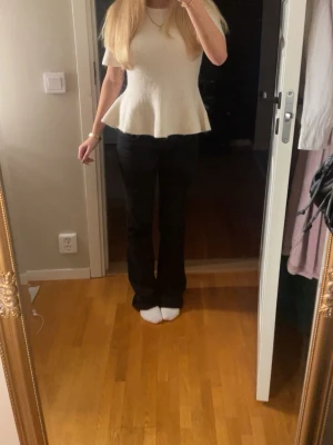 Vit ribbad topp med volang - Säljer en vit ribbad topp med korta ärmar och volang nertill. Toppen har en figurnära passform upptill och släpper ut vid midjan för en snygg siluett. Perfekt att styla med jeans eller kjol för en trendig look.